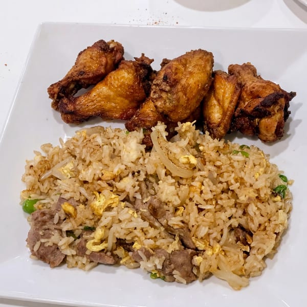 Golden-brown fried chicken wings and beef fried rice with egg and peas on a white plate.