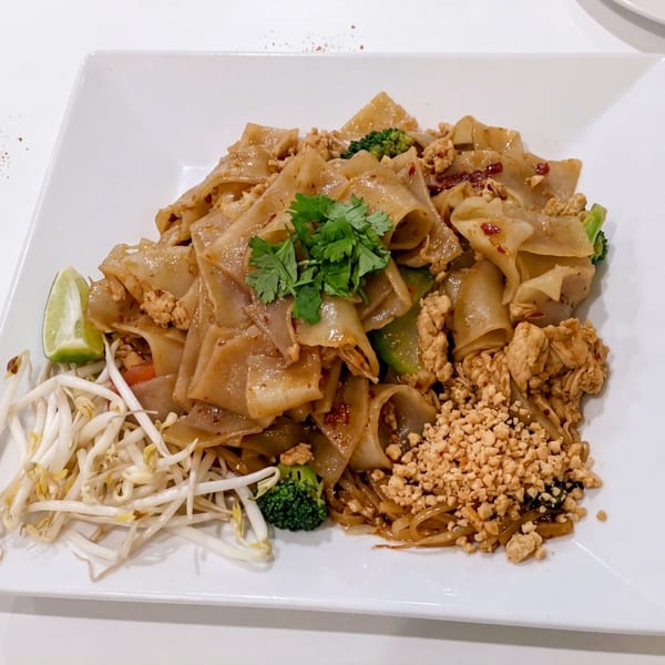 Pad See Ew with chicken, broccoli, bean sprouts, lime, and crushed peanuts on a white plate.