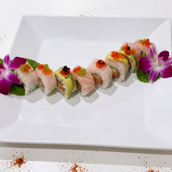Sushi rolls with avocado, salmon, and roe, garnished with purple orchids on a white plate.