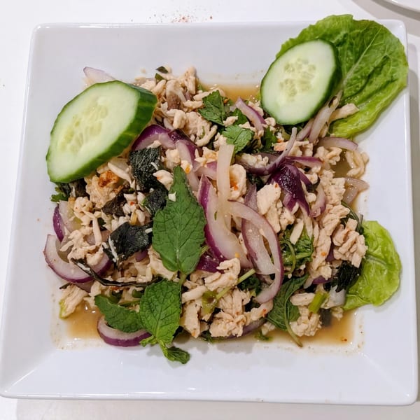 Larb Gai, a Thai chicken salad with red onions, mint, and cucumbers on a white plate.