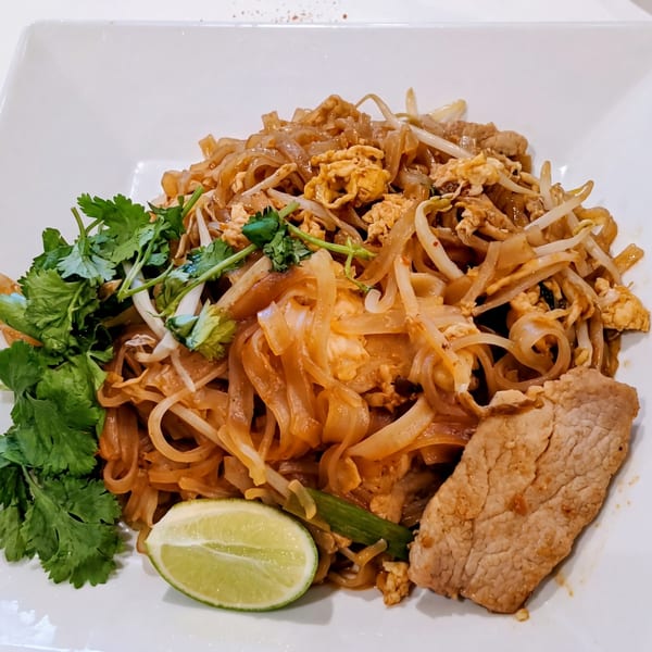 Pad See Ew with beef, scrambled egg, bean sprouts, cilantro, and a lime wedge on a white plate.