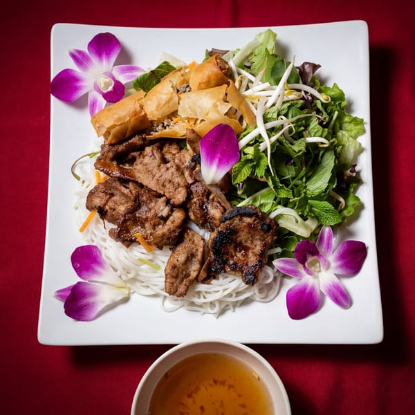 Vietnamese vermicelli noodles with grilled pork, crispy spring rolls, fresh herbs, and bean sprouts, garnished with orchids.