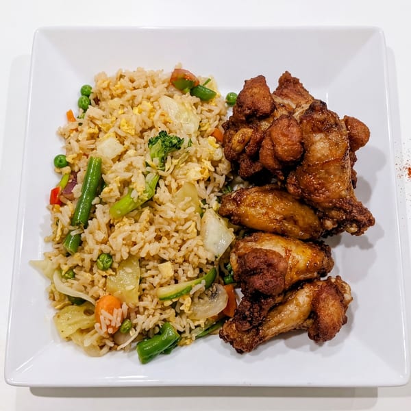 A white square plate with fried rice and vegetables next to crispy fried chicken wings.