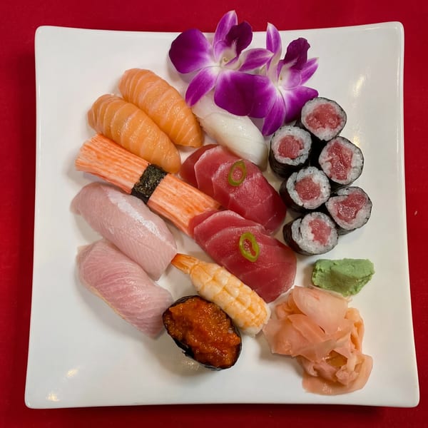 A white rectangular plate filled with various sushi and sashimi, garnished with purple orchids.